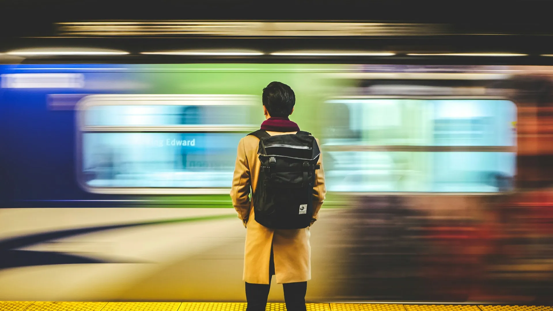 Un voyageur attend seul sur un quai de métro, avec son sac à dos
